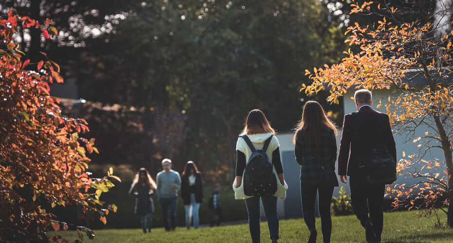 Various students walking across campus with autumn leaves on the trees