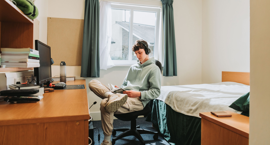 male stuent in bedroom listening to music with headphones